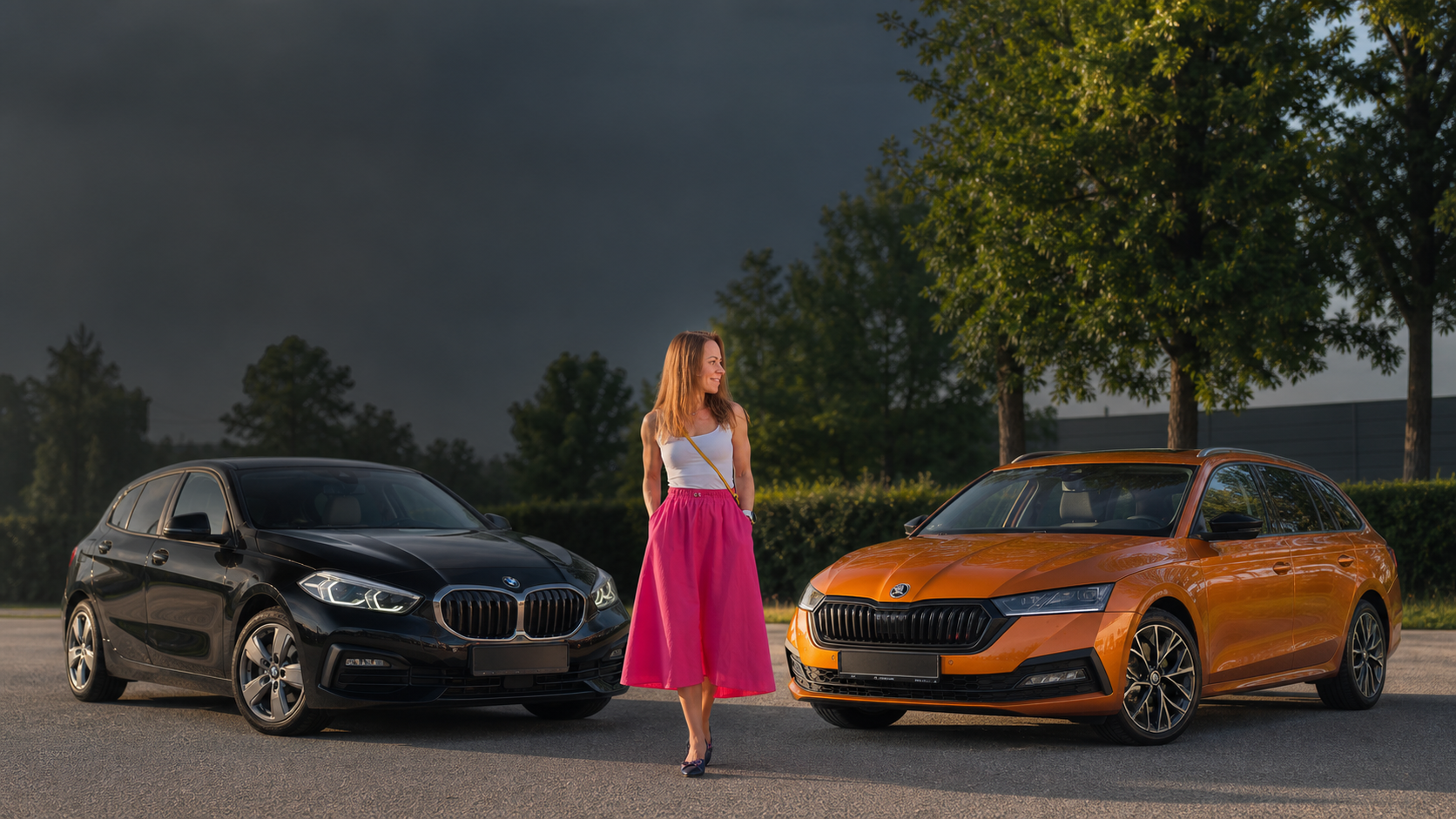 Naine seisab musta BMW 118i ja oranži Škoda Octavia Combi vahel ning võrdleb neid